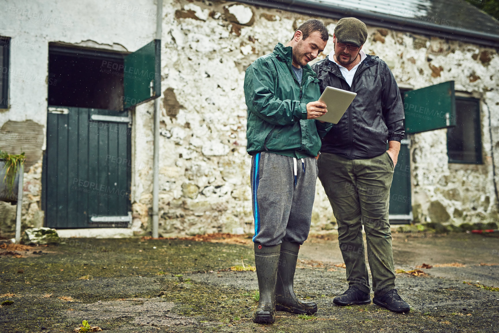 Buy stock photo Shot of two cheerful young farmers busy on a digital tablet while standing outside on a farm during the day