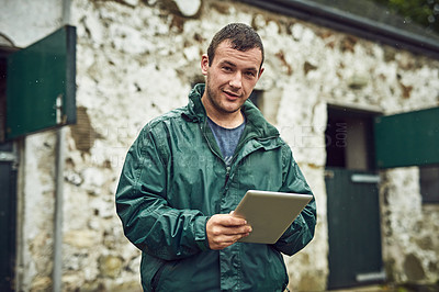 Buy stock photo Portrait of a cheerful young farmer busy on a digital tablet while standing outside on a farm during the day