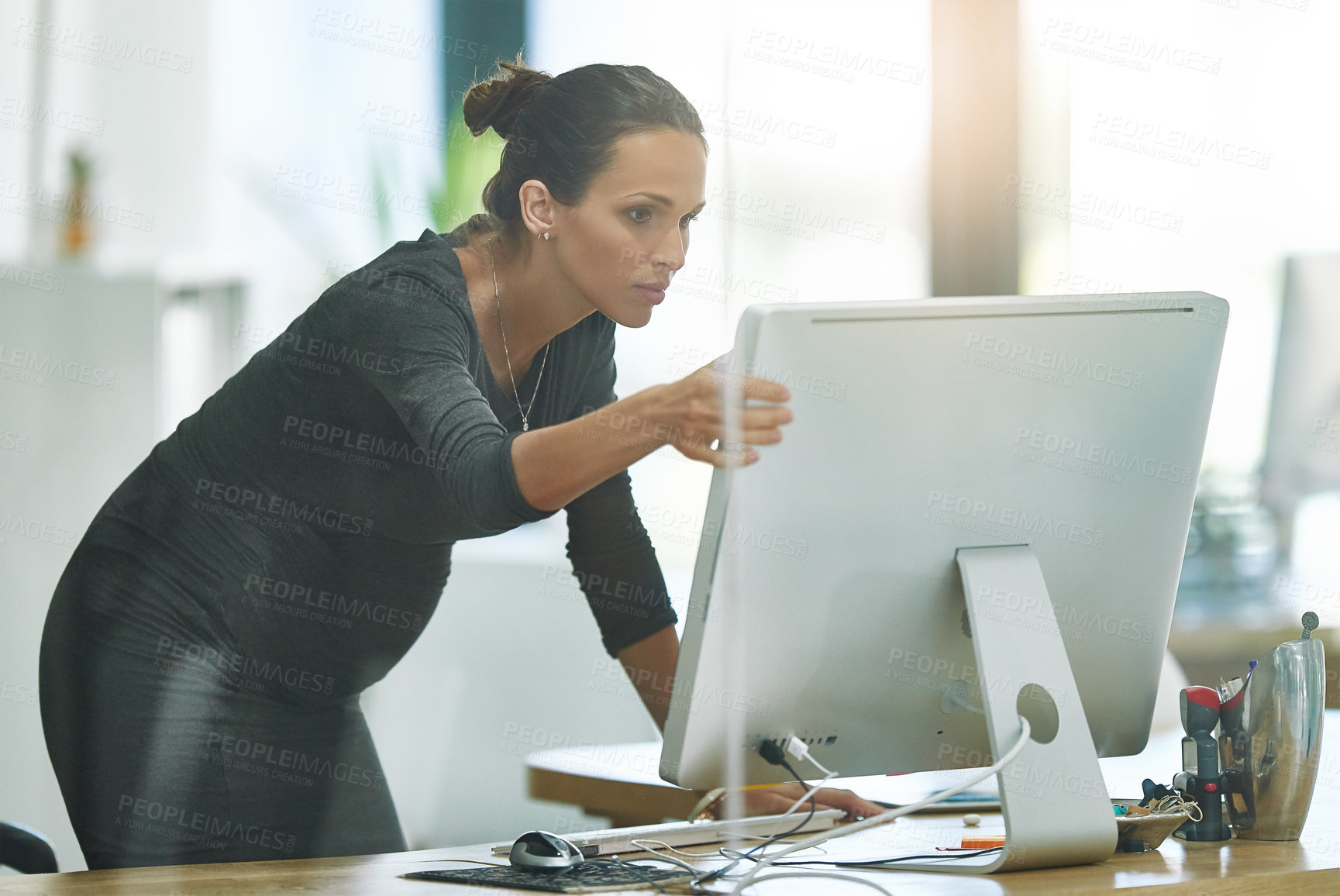 Buy stock photo Shot of a pregnant businesswoman looking at something on her computer while working in the office