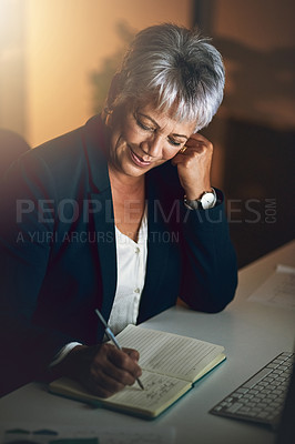 Buy stock photo Shot of a mature businesswoman writing in a notebook during a late night at work
