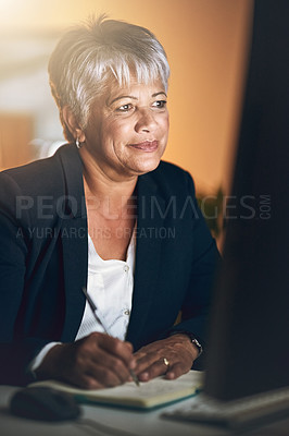 Buy stock photo Shot of a mature businesswoman writing in a notebook and using a computer during a late night at work