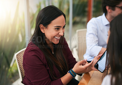 Buy stock photo Shot of a cheerful young woman holding her cellphone while talking to another person at a table outside