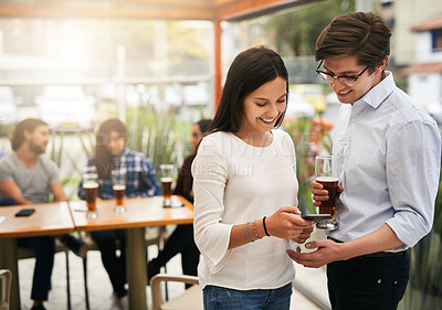Buy stock photo Shot of two cheerful young business work colleagues looking at photos on a phone outside at a restaurant