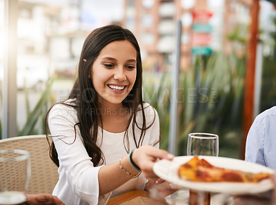 Buy stock photo Shot of a cheerful young woman receiving a slice of pizza while being seated next to a table at a restaurant outside