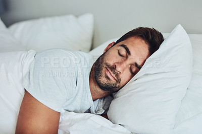 Buy stock photo Shot of a tired young man sleeping comfortably in his bed without a sign of being disturbed