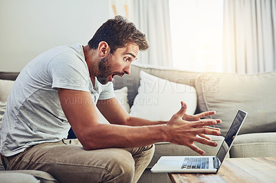 Buy stock photo Shot of a frustrated young man looking at his laptop surprised while sitting on the couch at home