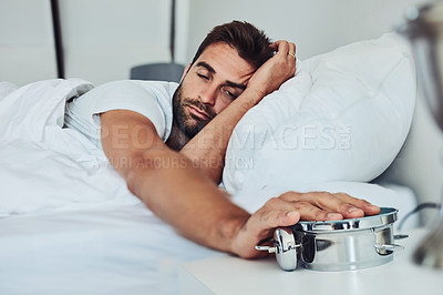 Buy stock photo Shot of a tired young man sleeping is his bed while holding a alarm clock after getting woken up from it