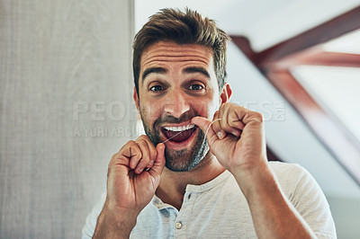 Buy stock photo Portrait of a cheerful young man flossing his teeth while looking at his reflection in the mirror at home