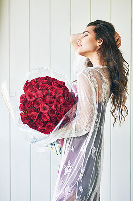 Buy stock photo Shot of a beautiful young woman standing with her eyes closed while holding a bouquet of roses outside during the day