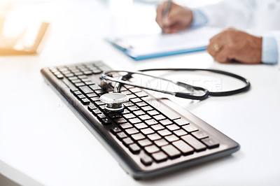 Buy stock photo Shot of a keyboard with a stethoscope on it while an unrecognizable man writes on a form in the background
