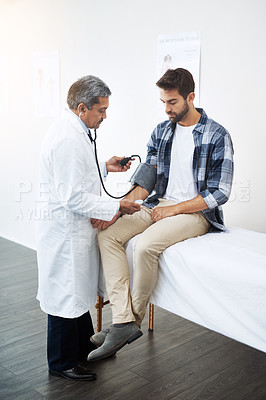 Buy stock photo Shot of a mature male doctor doing a check up on a young patient who's seated on a doctor's bed