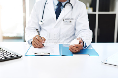 Buy stock photo Shot of an unrecognizable male doctor writing on a form while holding medication in his office