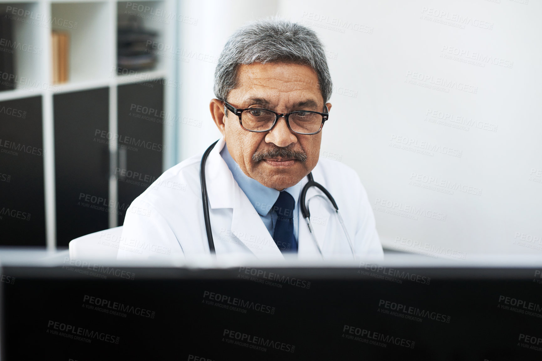 Buy stock photo Shot of a focused mature male doctor working on a computer while being seated in his office during the day