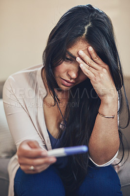 Buy stock photo Shot of a young woman looking worried while taking a pregnancy test at home