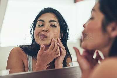 Buy stock photo Shot of a young woman squeezing a pimple on her face at home
