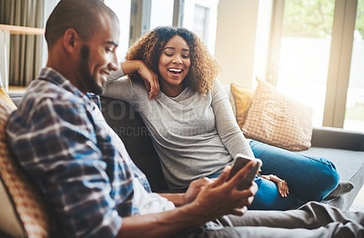 Buy stock photo Happy, laughing and cheerful couple relaxing together and looking at social media on a phone at home while sitting on the sofa inside. Young husband and wife enjoying browsing online on a sunny day