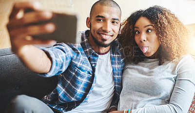 Buy stock photo Funny and silly couple taking selfie and making goofy face at phone for social media post while relaxing. Boyfriend and girlfriend having fun and enjoying time together at home and sharing it online