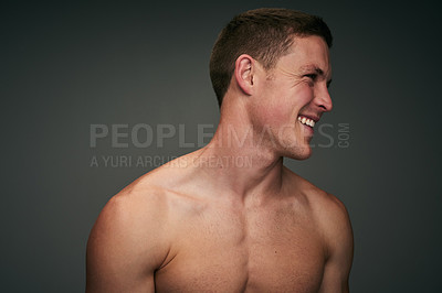 Buy stock photo Studio shot of a cheerful young shirtless man standing against a grey background while looking down