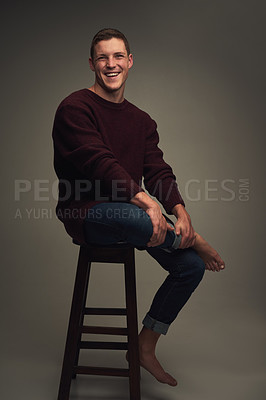 Buy stock photo Studio portrait of a cheerful young man seated against a grey background while looking at the camera