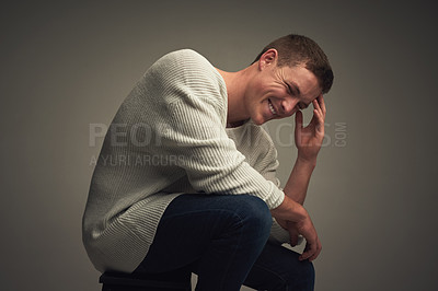 Buy stock photo Studio portrait of a cheerful young man seated against a grey background while looking at the camera