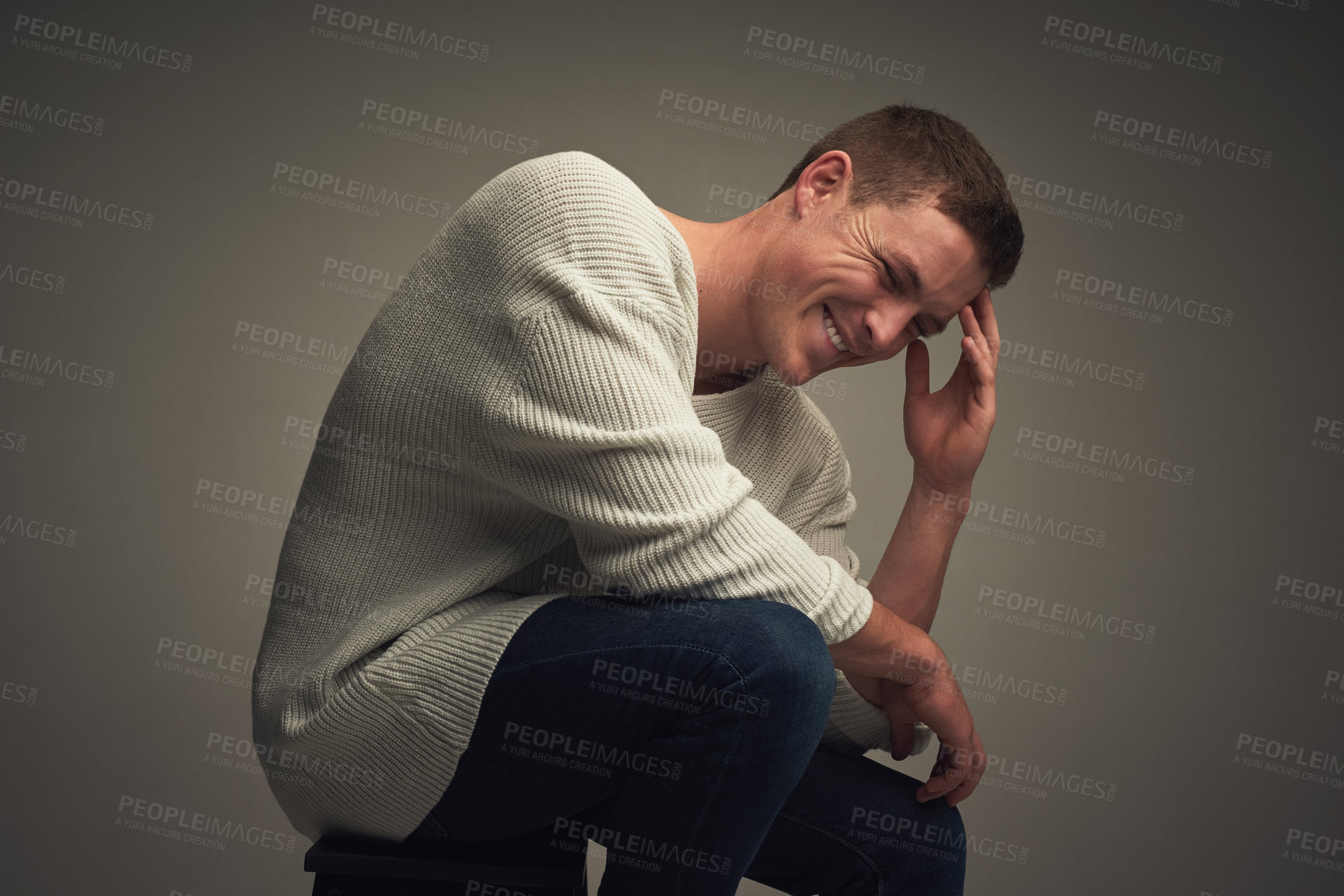 Buy stock photo Studio portrait of a cheerful young man seated against a grey background while looking at the camera