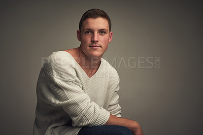 Buy stock photo Studio portrait of a confident young man seated against a grey background while looking at the camer
