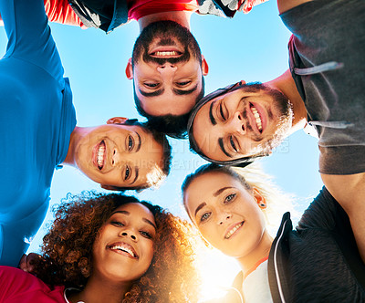 Buy stock photo Low angle shot of a group of young cheerful friends standing with their heads together while looking into the camera