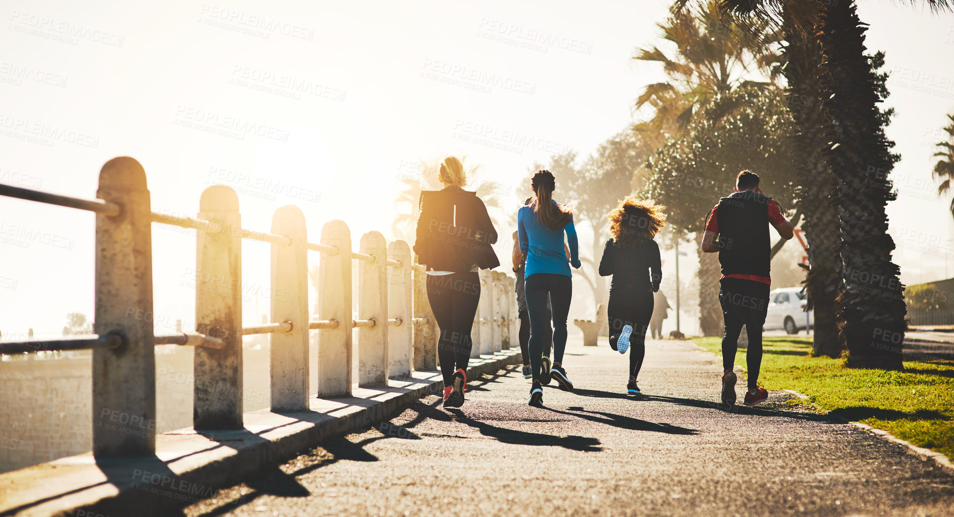 Buy stock photo Rearview shot of a fitness group out running on the promenade