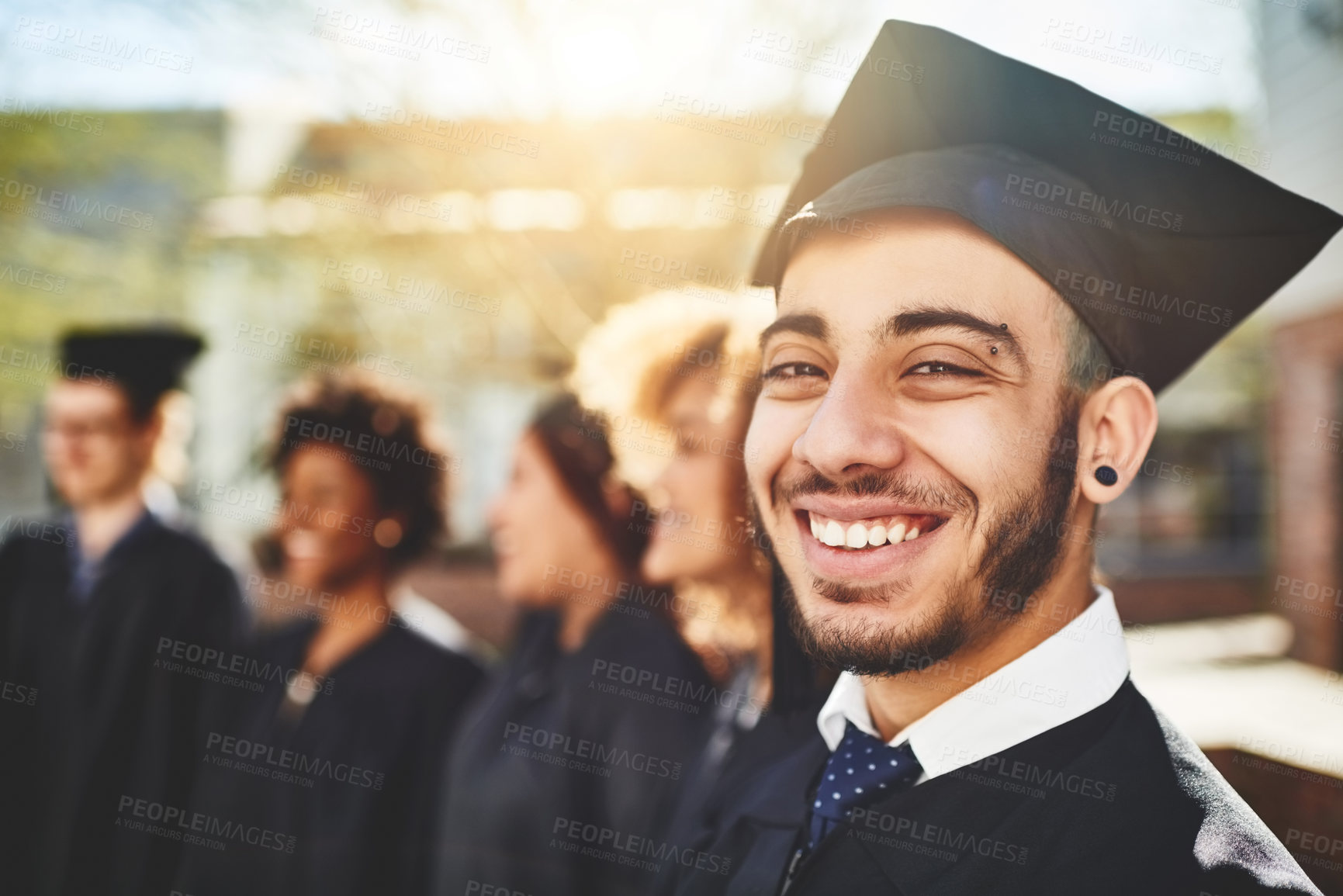 Buy stock photo Happy man, portrait and graduation with cap for outdoor ceremony, achievement or milestone at campus. Male person, graduate or group of students with smile for celebration or future at university