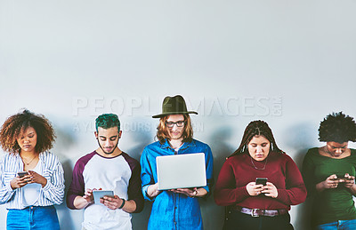 Buy stock photo Studio shot of a group of young people standing against a wall and using wireless technology