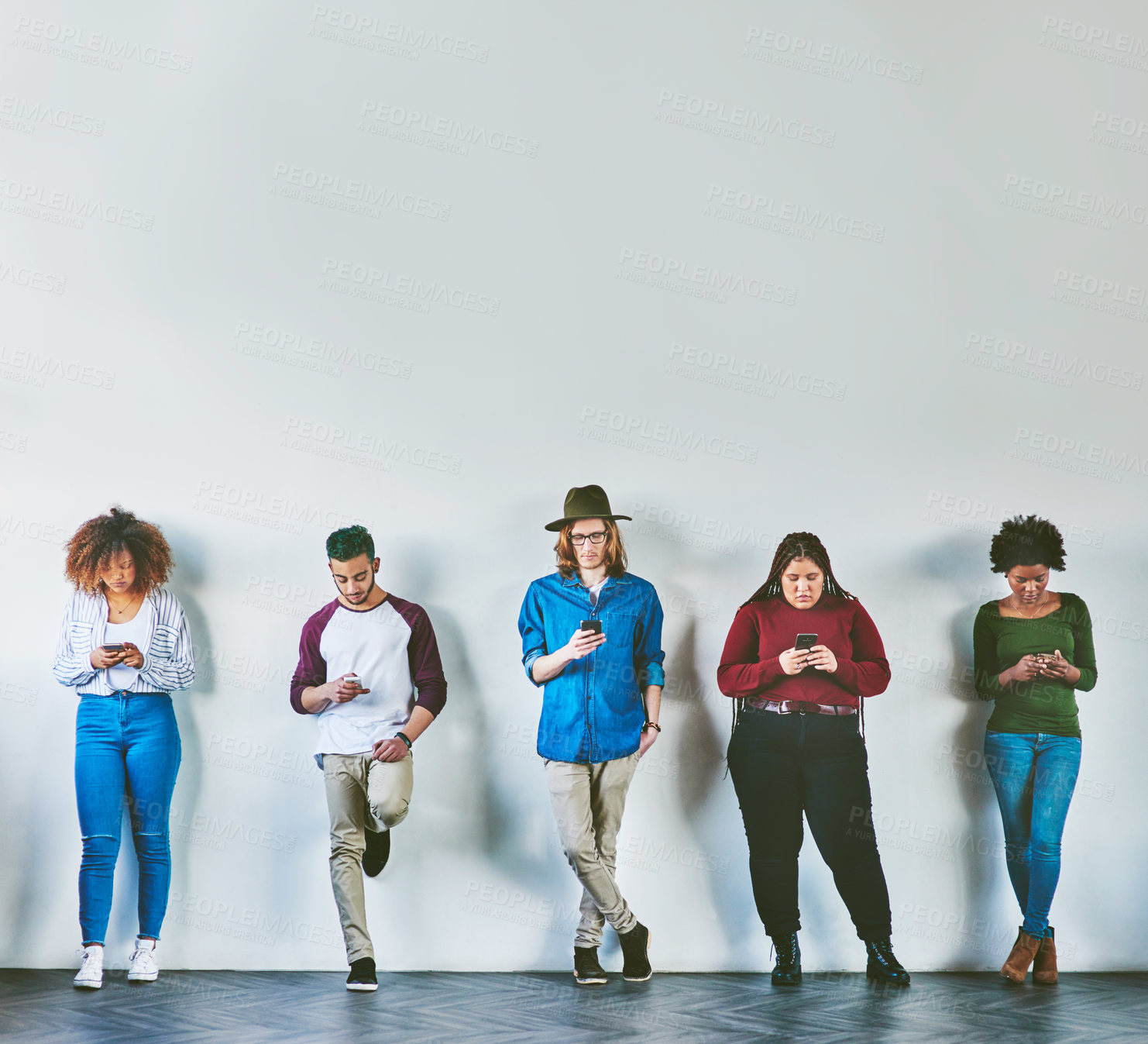 Buy stock photo Studio shot of a group of young people standing against a wall and using their mobile phones