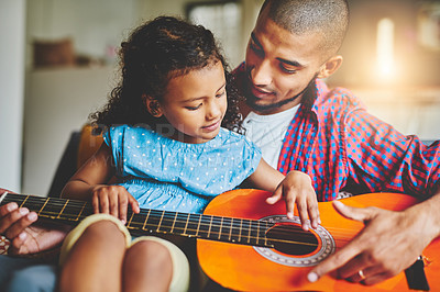 Buy stock photo Shot of an adorable little girl and her father playing a guitar together on the sofa at home