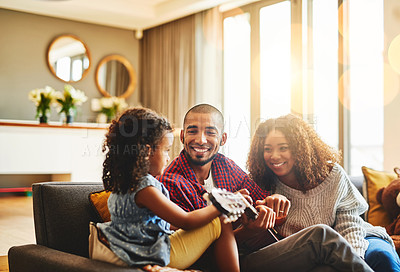 Buy stock photo Shot of an adorable little girl and her parents playing a guitar together on the sofa at home