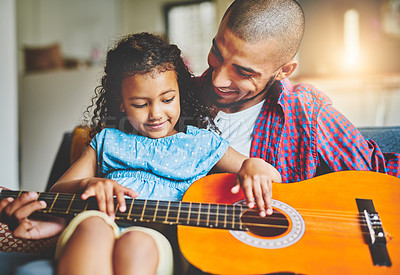 Buy stock photo Shot of an adorable little girl and her father playing a guitar together on the sofa at home