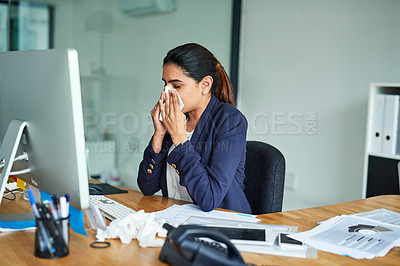 Buy stock photo Shot of a young businesswoman blowing her nose while working in an office