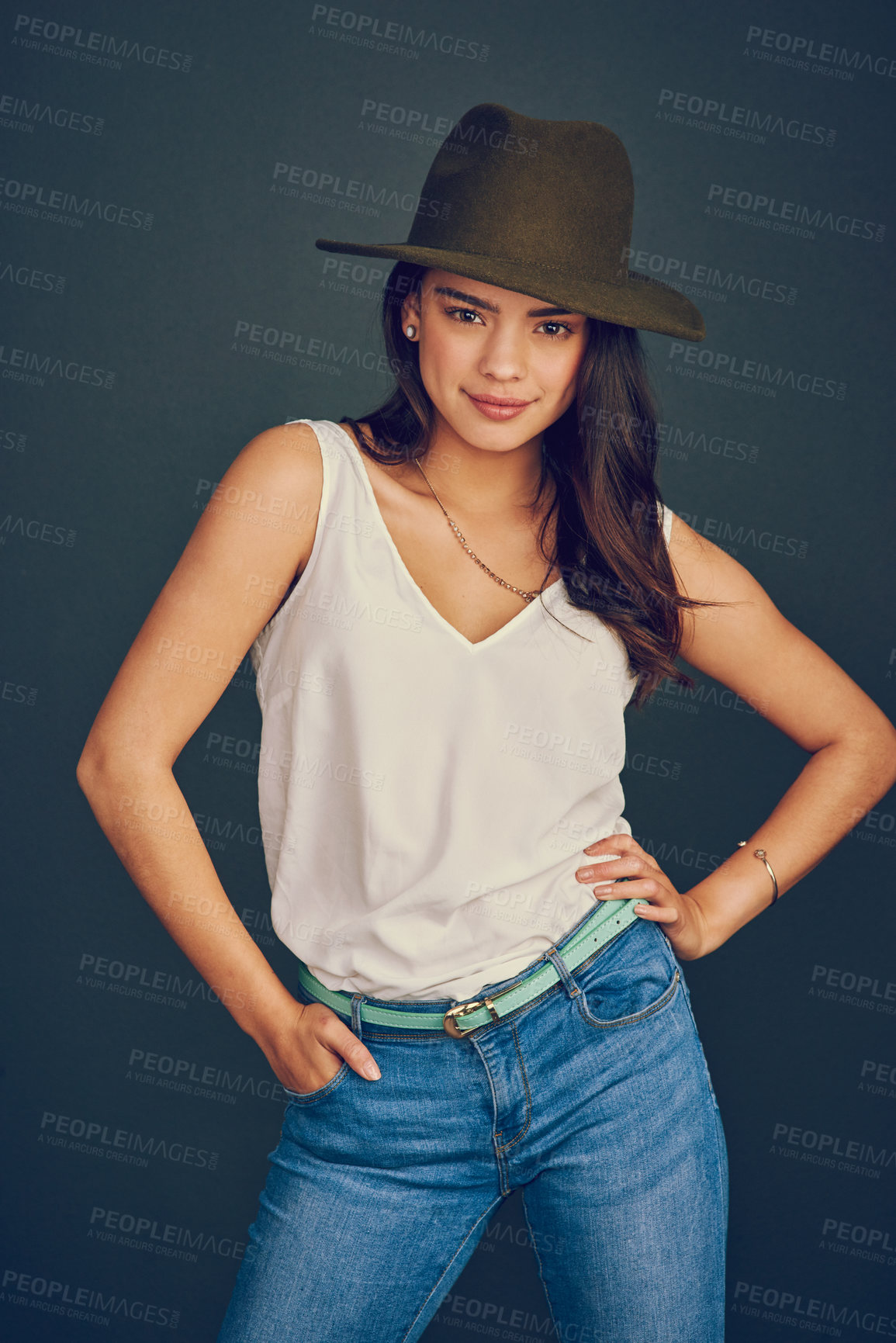 Buy stock photo Studio shot of an attractive young woman wearing a hat and posing while standing against a dark background