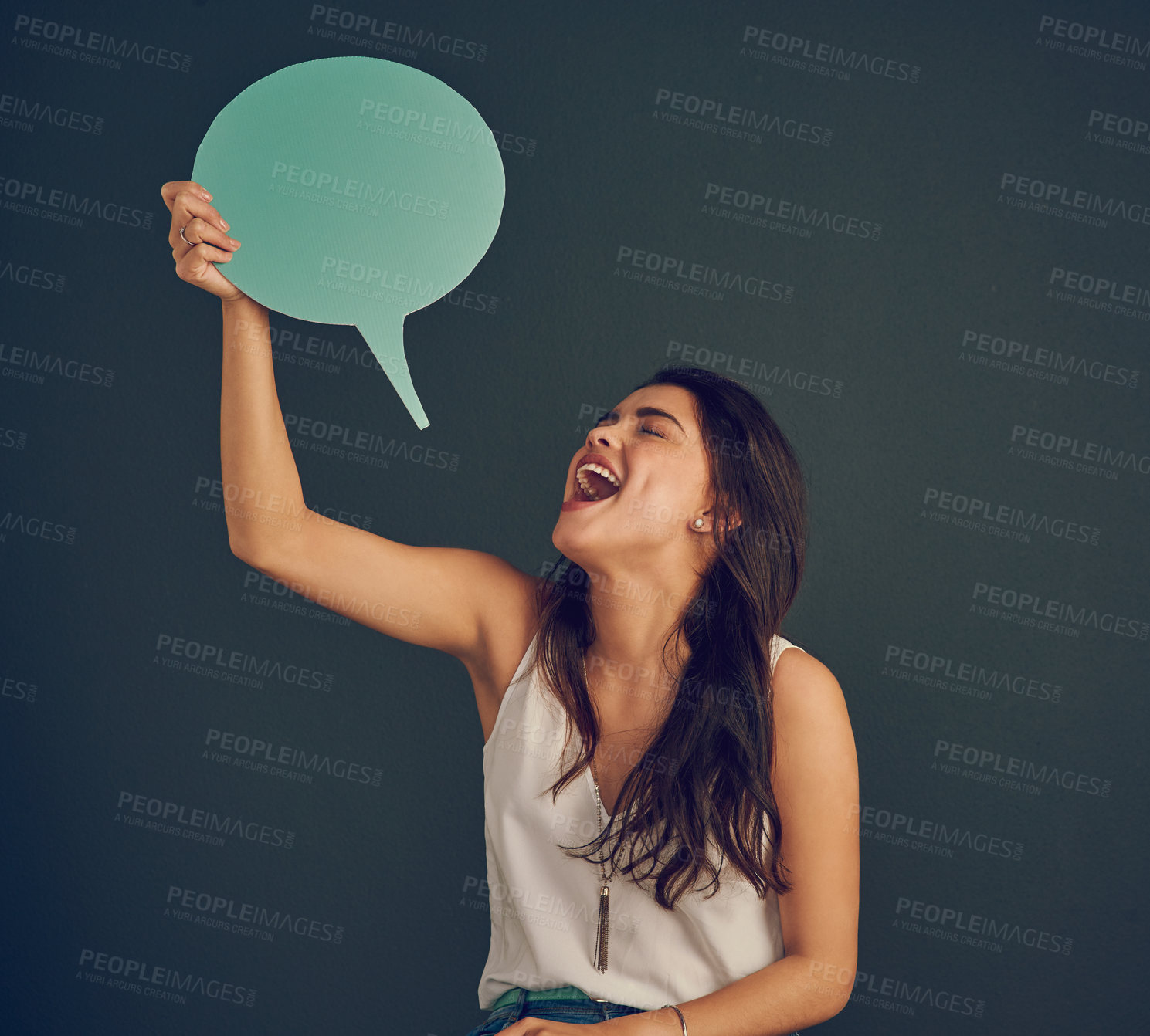 Buy stock photo Studio shot of a cheerful young woman holding up a speech bubble while standing against a dark background