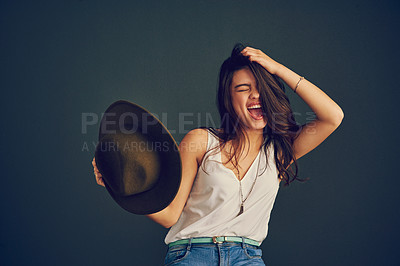 Buy stock photo Studio shot of a cheerful young woman holding her head with one hand and holding a hat with the other