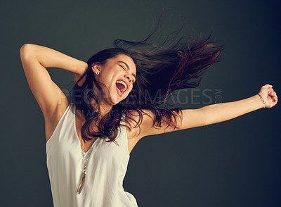 Buy stock photo Studio shot of a carefree young woman shouting with her arms raised and her hair blowing against a dark background