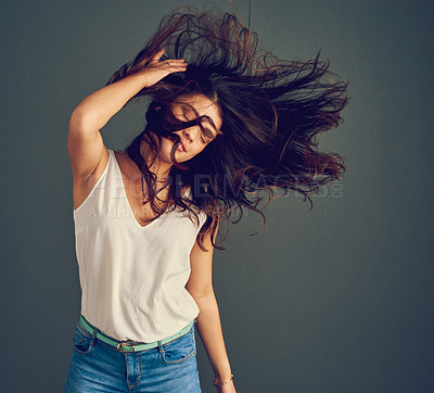 Buy stock photo Studio shot of a carefree young woman holding her hair while it gets blown by wind as she stands against a dark background
