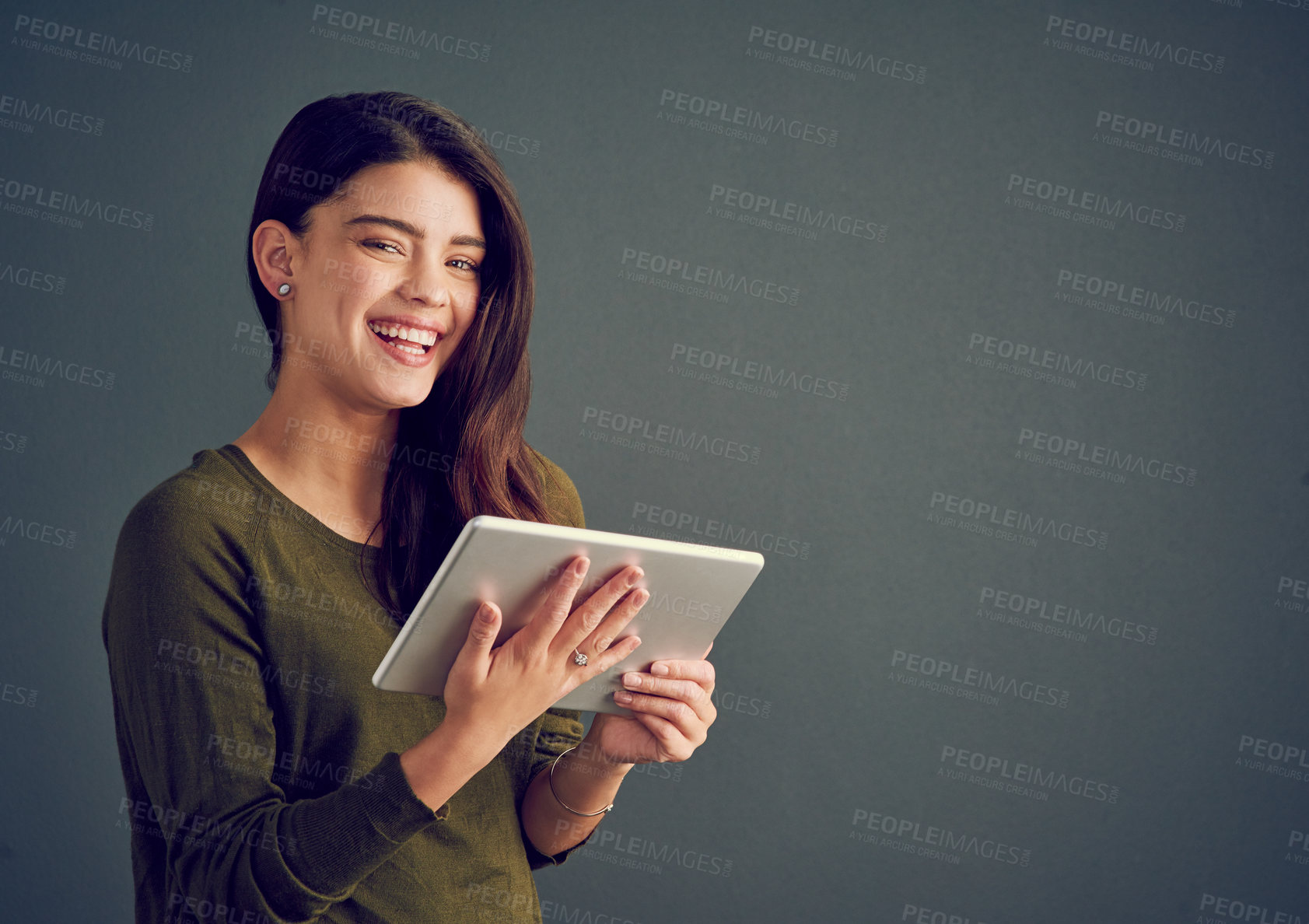 Buy stock photo Studio shot of an cheerful young woman holding a digital tablet while standing against a dark background