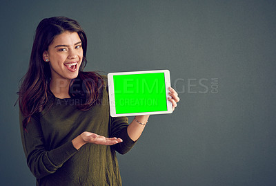 Buy stock photo Studio shot of an cheerful young woman holding a digital tablet while standing against a dark background