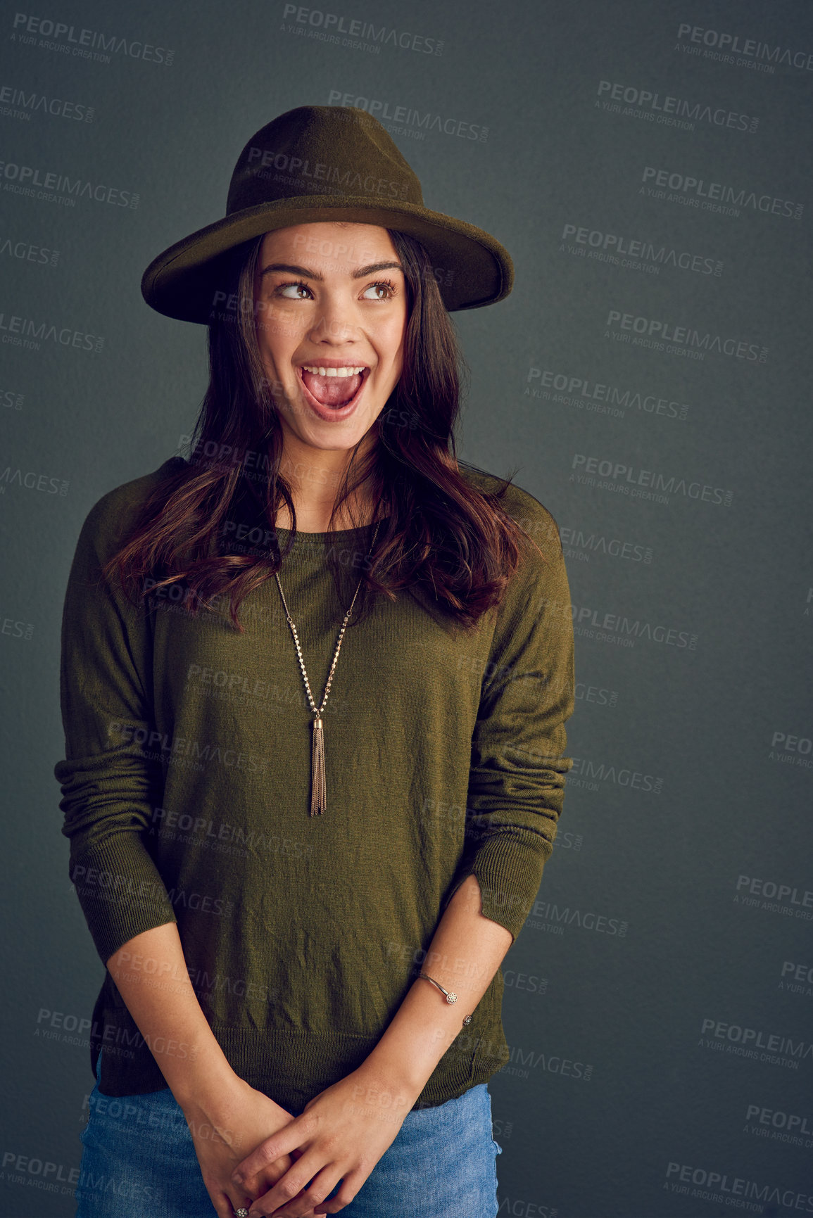 Buy stock photo Studio shot of a carefree young woman posing with a hat while standing against a dark background