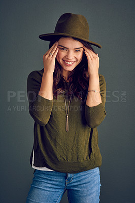 Buy stock photo Studio shot of a cheerful young woman posing with a hat while standing against a dark background