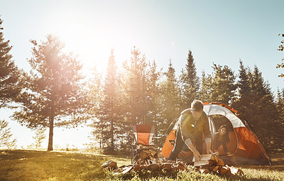 Buy stock photo Couple, campfire and nature with wood by tent on grass field for outdoor vacation, holiday or weekend. Young man preparing fire with woman for camping, leisure or summer getaway in sunshine at forest