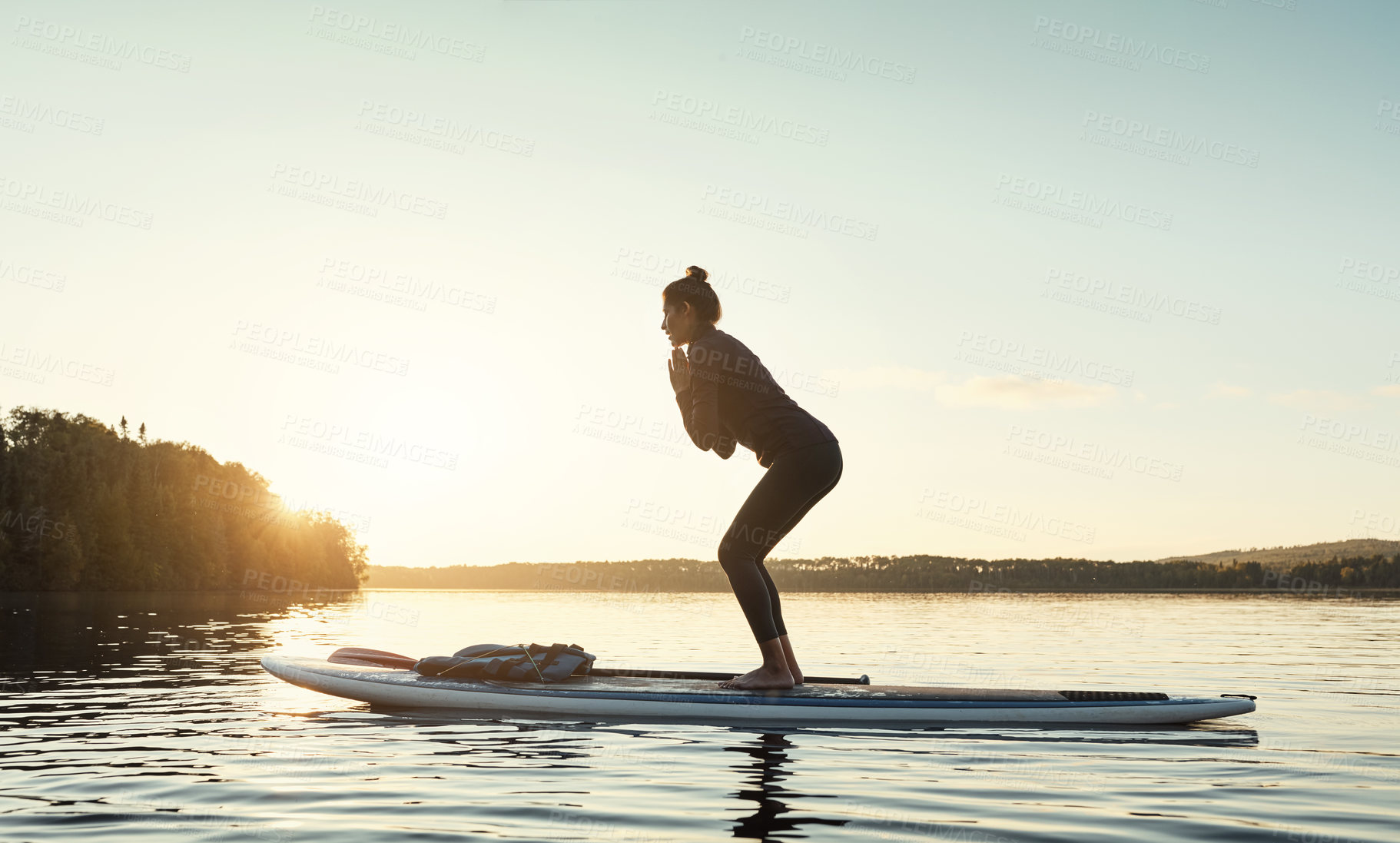Buy stock photo Shot of an attractive young woman doing yoga on a paddle board on a lake outdoors