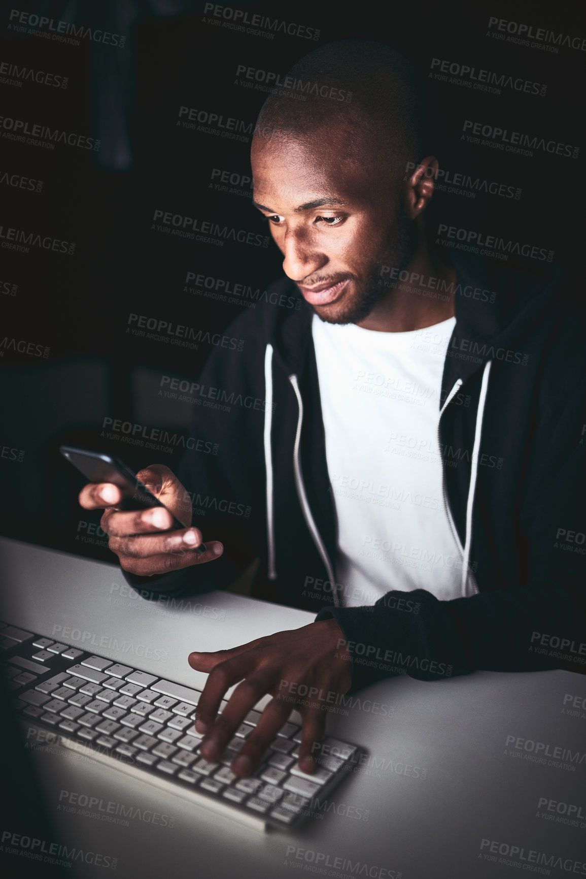 Buy stock photo High angle shot of a young man using his cellphone while working late in the office