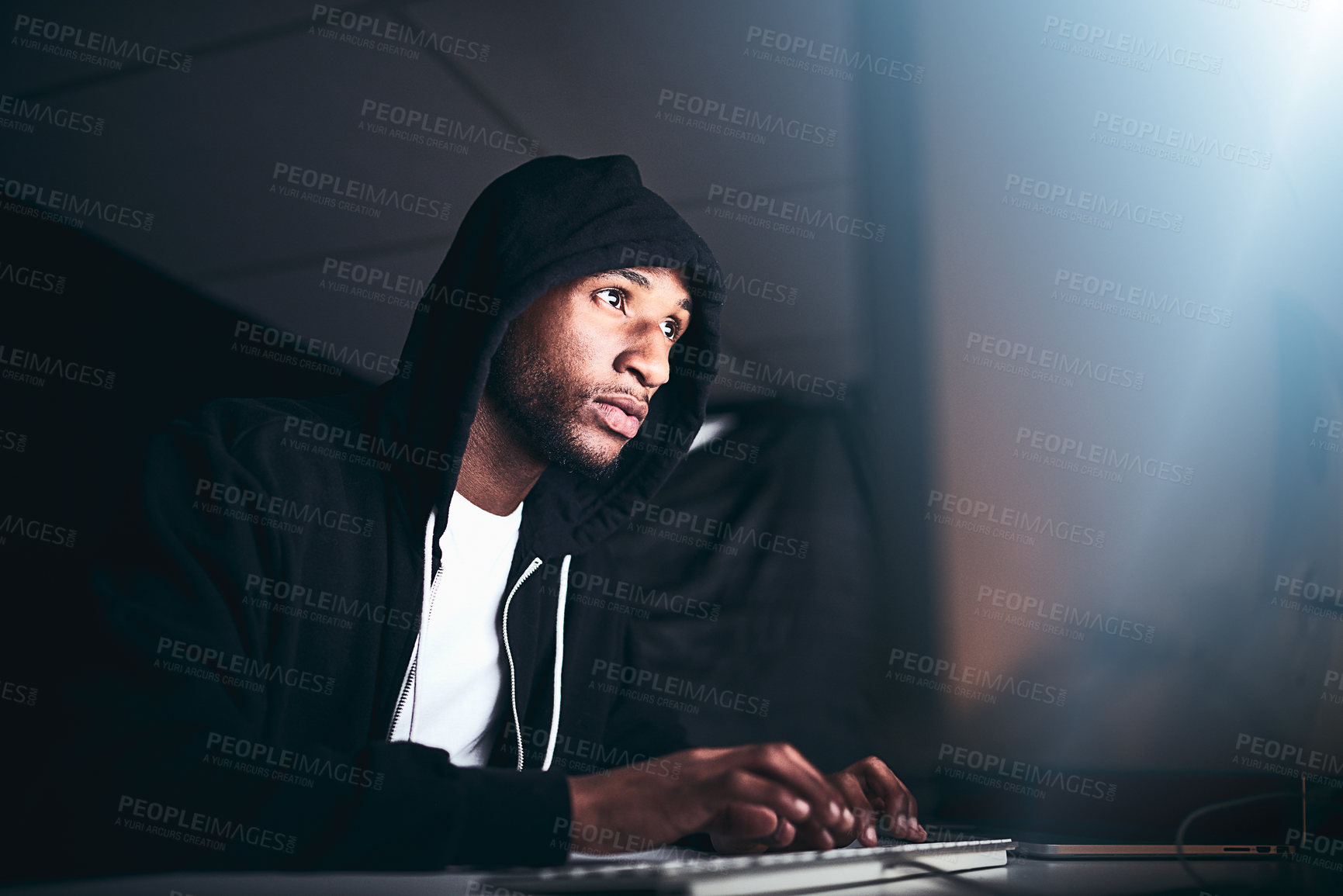 Buy stock photo Low angle shot of a young male hacker cracking a computer code in the dark