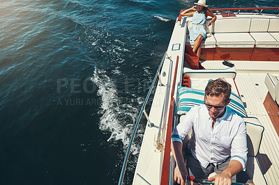 Buy stock photo High angle shot of a handsome young man steering a yacht with his wife sitting in the background