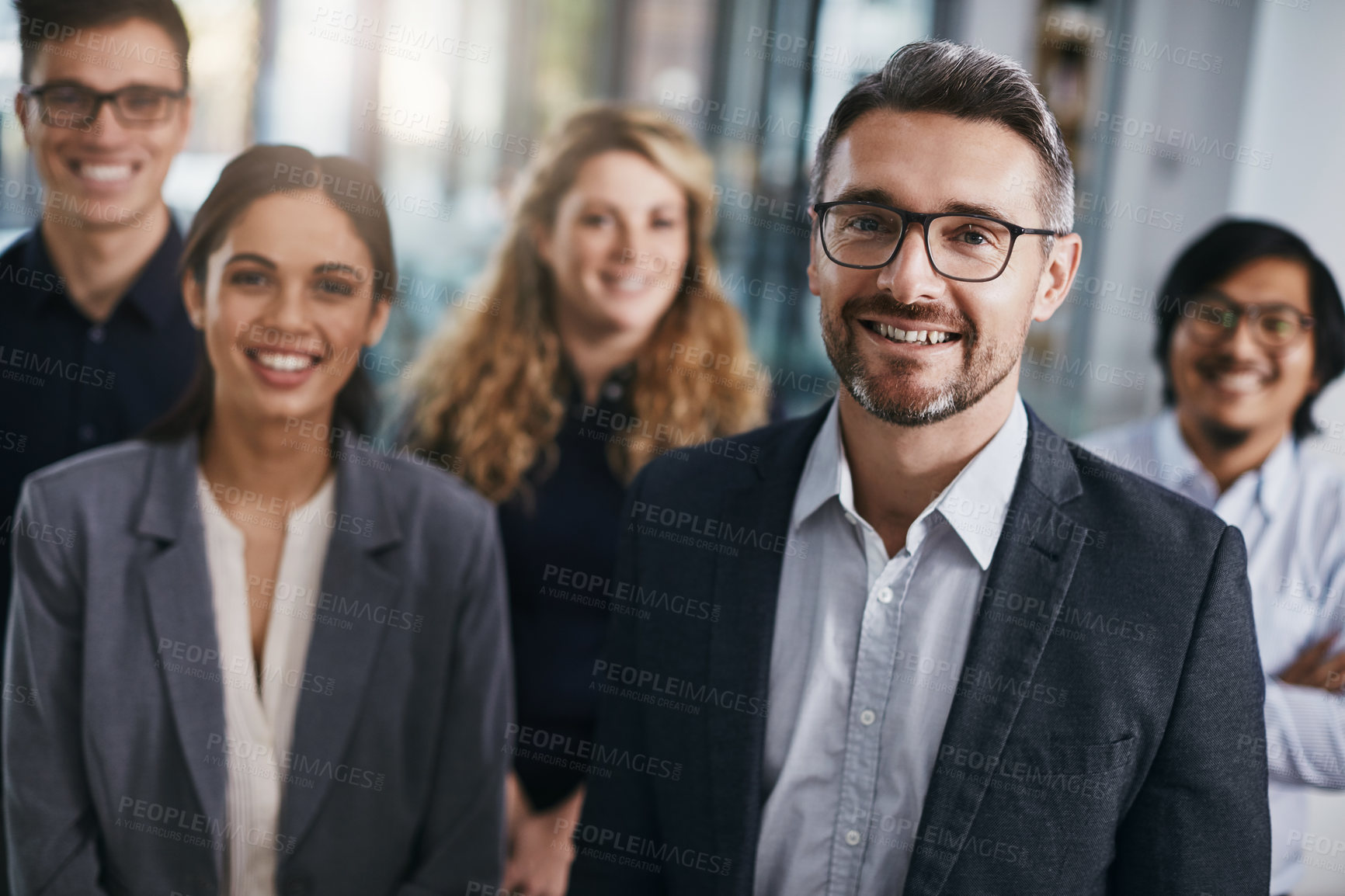 Buy stock photo Portrait of a mature businessman standing in an office with his colleagues in the background